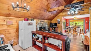 Ein gemütliches Blockhauss-Interieur mit Holzbalkendecke, Essbereich und einer Küche mit Kühlschrank und Herd.