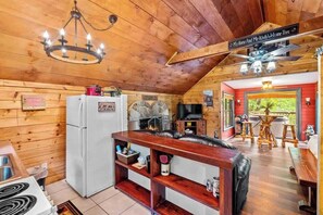 Ein gemütliches Blockhauss-Interieur mit Holzbalkendecke, Essbereich und einer Küche mit Kühlschrank und Herd.