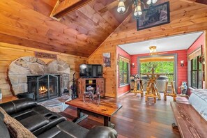 A cozy cabin interior with a stone fireplace, a television, and a dining area.