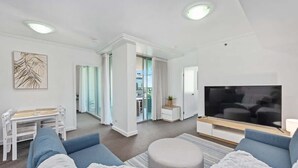 A modern living room with a sofa, TV, and a dining area with chairs and a table.