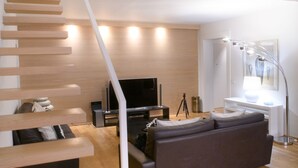 Ein modernes Wohnzimmer mit einer Holztreppe, einer Couch, einem Flachbildfernseher und einem Schreibtisch mit einer Lampe.