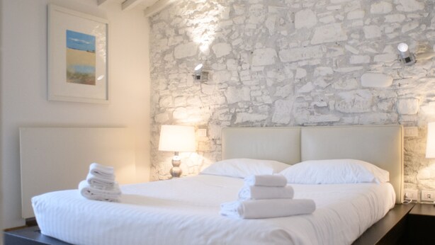Ein Schlafzimmer mit Steinwand, Holzbalkendecke, einem Bett mit weißer Bettwäsche und zwei Nachttischlampen.