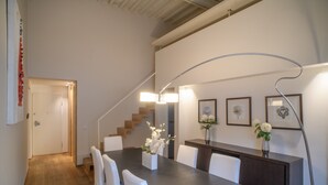 Ein moderner Essbereich mit einem langen Tisch, weißen Stühlen und einem Blumenstrauß.