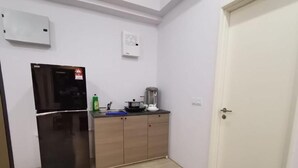 A compact kitchen with a black refrigerator, wooden cabinets, a countertop with a kettle, and a door to the right. - Pavilion Bukit Jalil @ REVO Cozy Studio Suite (Kuala Lumpur)