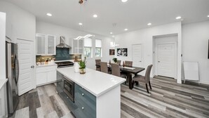 A modern kitchen with white cabinetry, a central island, and a dining area with a table and chairs. - EaDo Signature - East of Downtown Spacious Home (Houston)