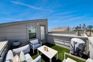 A rooftop terrace with a city skyline view, a covered grill, outdoor seating, and a small table with a potted plant. - EaDo Signature - East of Downtown Spacious Home (Houston)
