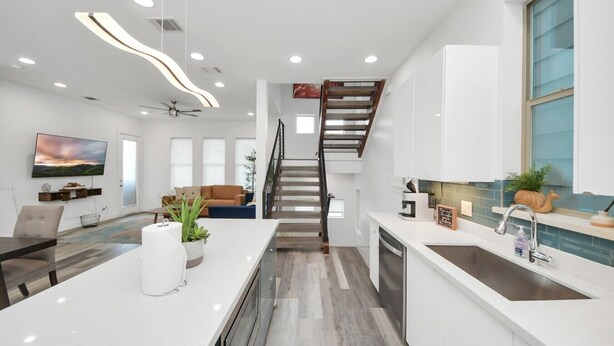 A modern kitchen with a central island, a dining area with a sofa, and a staircase leading to another level. - EaDo Signature - East of Downtown Spacious Home (Houston)