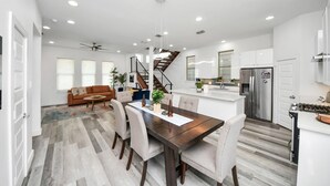 A modern kitchen with a central island, a dining area with a wooden table, and a staircase leading to an upper level. - EaDo Signature - East of Downtown Spacious Home (Houston)