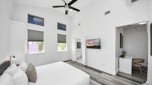 A bedroom with a bed, a ceiling fan, a TV, and a desk with a chair. - EaDo Signature - East of Downtown Spacious Home (Houston)
