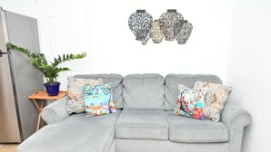 A grey sectional sofa with colorful patterned cushions, a potted plant, and decorative wall art.