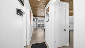 Ein Flur mit weißen Wänden, einer Holzbodenverkleidung und einer schwarzen Fußmatte. An der Wand hängen gerahmte Bilder und ein Schild.
