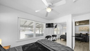 Ein Schlafzimmer mit Bett, Deckenventilator, Fernseher und einem großen Fenster.