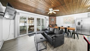 Ein modernes Wohnzimmer mit Holzboden, einem grauen Sofa, einem Esstisch und einer Küchenzeile mit Kühlschrank.