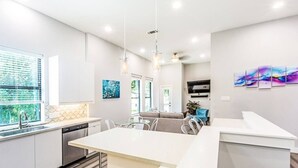 Eine moderne Küche mit einer zentralen Kochinsel, ein Essbereich mit einer Couch und ein Wohnzimmer mit Fernseher.
