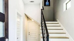 Una escalera con barandilla negra, suelo de madera y una puerta blanca al final.