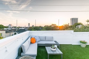 A rooftop terrace with a grey sofa, a small table, and a potted plant.