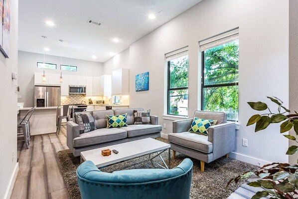 A modern living room with a sofa set, a coffee table, and a dining area with a kitchen in the background.
