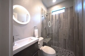 A modern bathroom with a double sink, toilet, and a glass-enclosed shower.