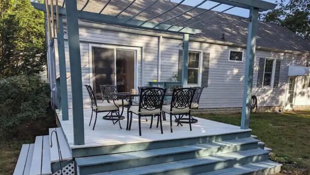 Een overdekt terras met een tafel en stoelen, een trap naar het huis en een garage.