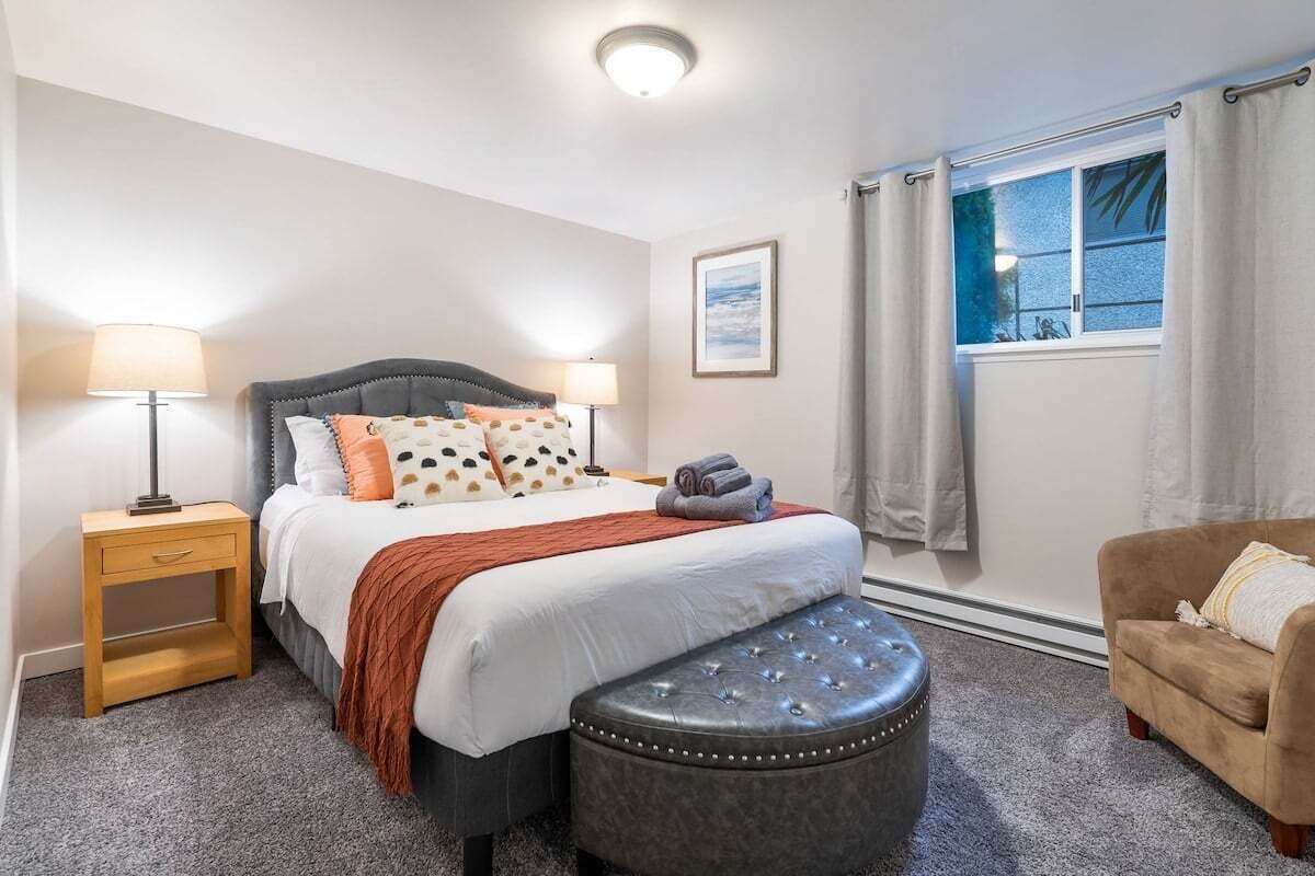 A bedroom with a bed, bedside tables, a window with curtains, a chair, and a wall-mounted artwork.