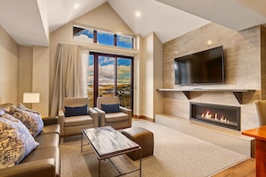 A modern living room with a fireplace, a flat-screen TV, and a large window with a view.