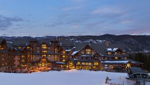 Un grand chalet comprenant plusieurs bâtiments, un terrain enneigé et des montagnes en arrière-plan.