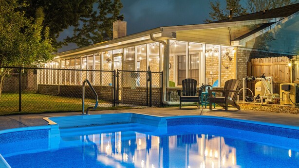 Ein Swimmingpool mit einer gläsernen Veranda, Gartenmöbeln und einem Holzzaun.