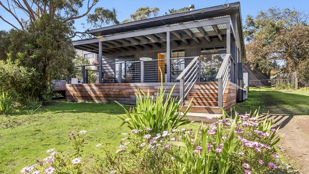 Una casa moderna con porche cubierto, escalera y un jardín bien cuidado con flores.