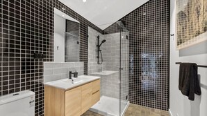 Un baño moderno con cabina de ducha de vidrio, un lavabo blanco y un mueble de tocador de madera.