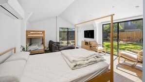 Un dormitorio moderno con una cama grande, un sofá, un televisor y vista al patio trasero.