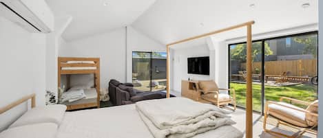 A modern bedroom with a large bed, a sofa, a TV, and a view of the backyard.