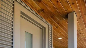 Una entrada moderna con puerta de cristal, reja metálica y techo de madera.