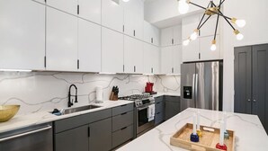 Una cocina moderna con armarios blancos, un refrigerador de acero inoxidable, una estufa a gas y una bandeja de madera con botellas.