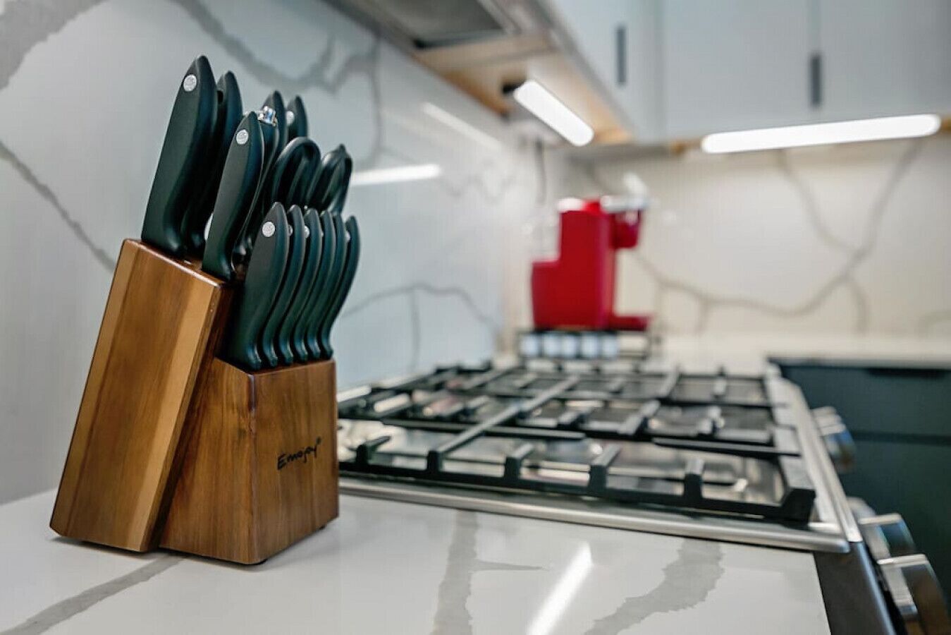 A kitchen with a gas stove, a knife block, and a marble backsplash.