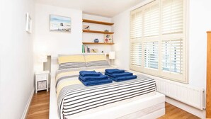 Una camera da letto con un letto, comodini, una finestra con persiane e uno scaffale con libri e oggetti decorativi.