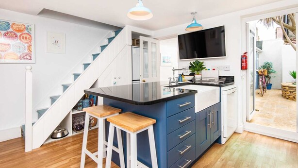 Una cucina moderna con isola centrale, sgabelli da bar, TV montata sopra l'isola e una scala che conduce a un altro livello.