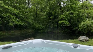 Uma banheira de hidromassagem rodeada por uma área arborizada, com um lago tranquilo ao fundo.
