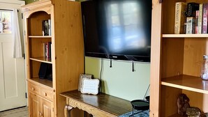 Una sala de estar con un mueble bajo de madera para el televisor, un televisor de pantalla plana, una estantería y una mesita con un jarrón y libros.