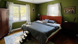 Un dormitorio con cama, ventilador de techo, mesita de noche, cómoda y ventana con cortinas.