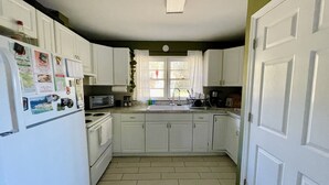 Una cocina compacta con gabinetes blancos, microondas, estufa y pileta.