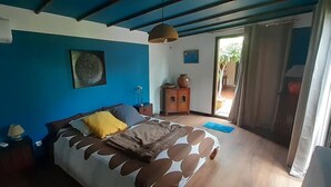 Une chambre à coucher avec un lit, une table de chevet, une lampe, une commode et une fenêtre avec des rideaux.