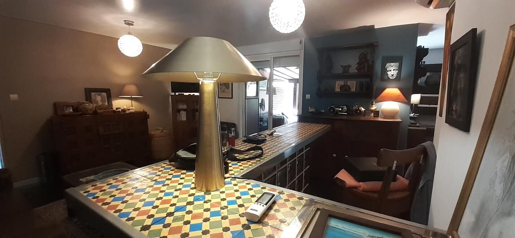 Et spiseområde med et ternet bord, en lampe og et barområde med hylder og en stol.