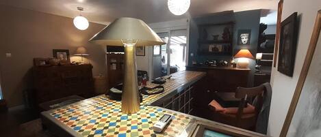 Et spiseområde med et ternet bord, en lampe og et barområde med hylder og en stol.