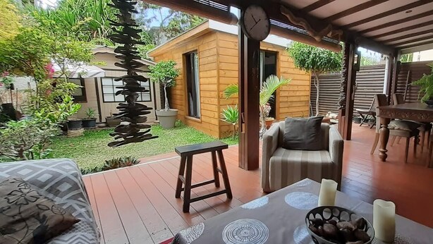 Une terrasse extérieure couverte, aménagée avec des meubles en bois, une petite table avec des bougies et une vue sur une maison en bois et un jardin.