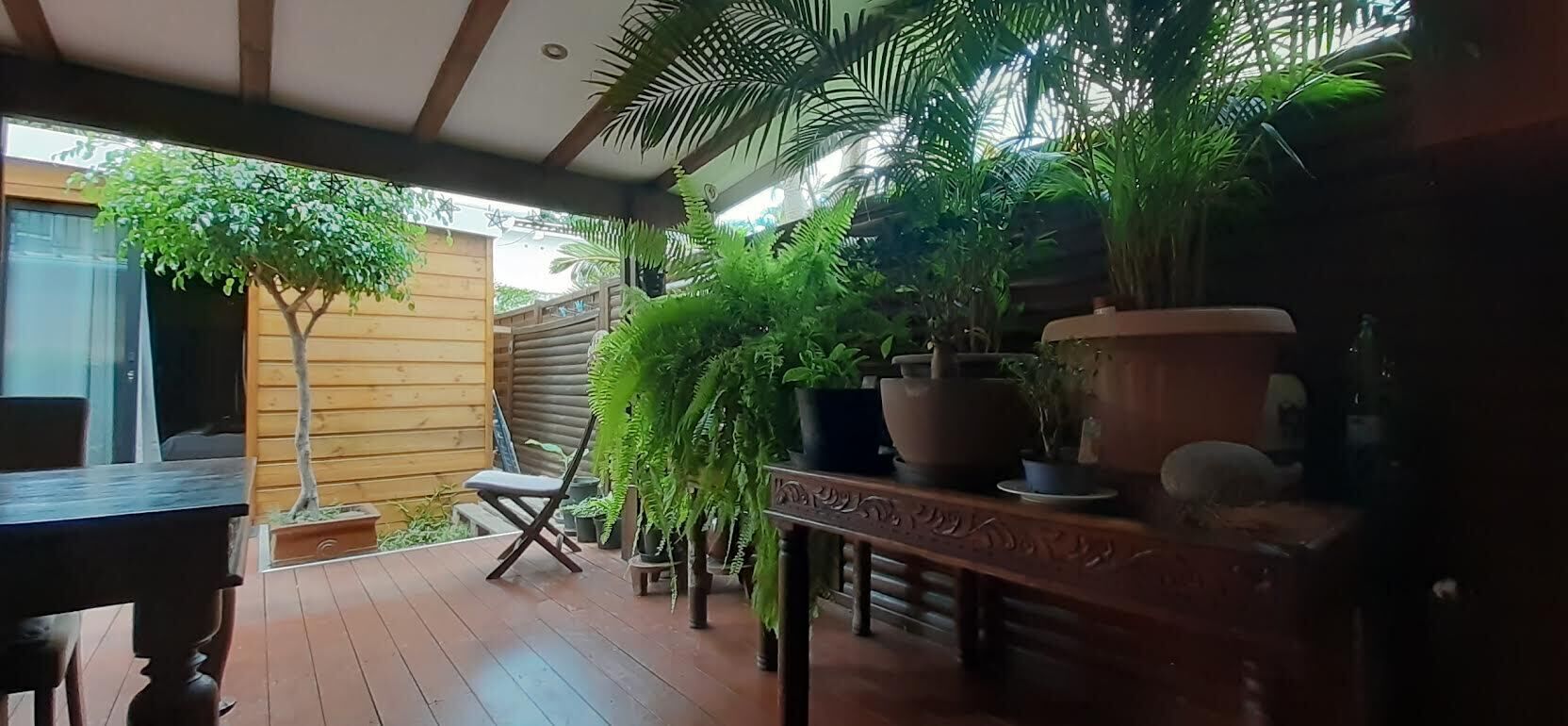 Una terraza de madera con una mesa y sillas para comer, rodeada de macetas y una jardinera grande.