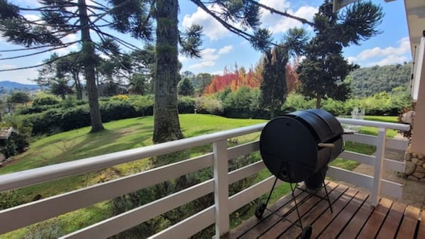 Ein Balkon mit Grill, weißer Brüstung und Blick auf eine grüne Landschaft mit Bäumen und einem entfernten Berg.