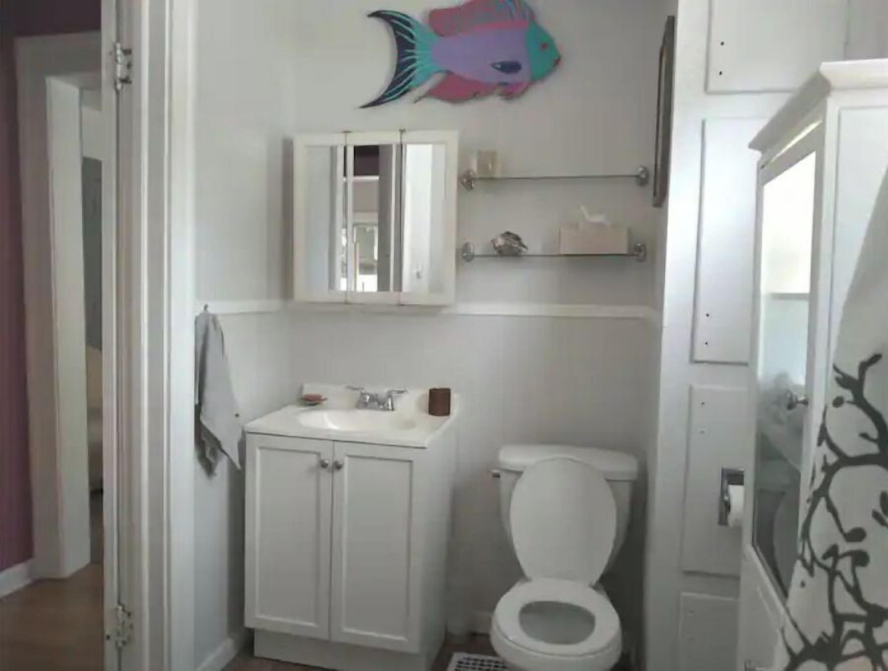 A small, white bathroom with a toilet, a sink with a mirror above it, and a shelf with toiletries.