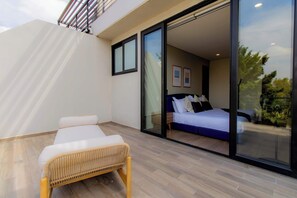 A modern bedroom with a large sliding glass door leading to a balcony, a bed with white bedding, and a wicker chair in the foreground. - Capitalia | Del Valle 2BR · Terrace & Parking (Ciudad de México)