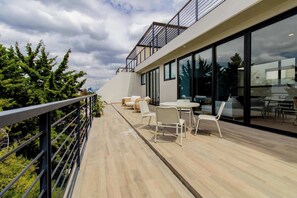 A modern outdoor deck with a railing, furnished with white chairs and a table, overlooking a forested area. - Capitalia | Del Valle 2BR · Terrace & Parking (Ciudad de México)