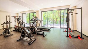 A gym with cardio machines, weightlifting equipment, and large windows offering a view of greenery.